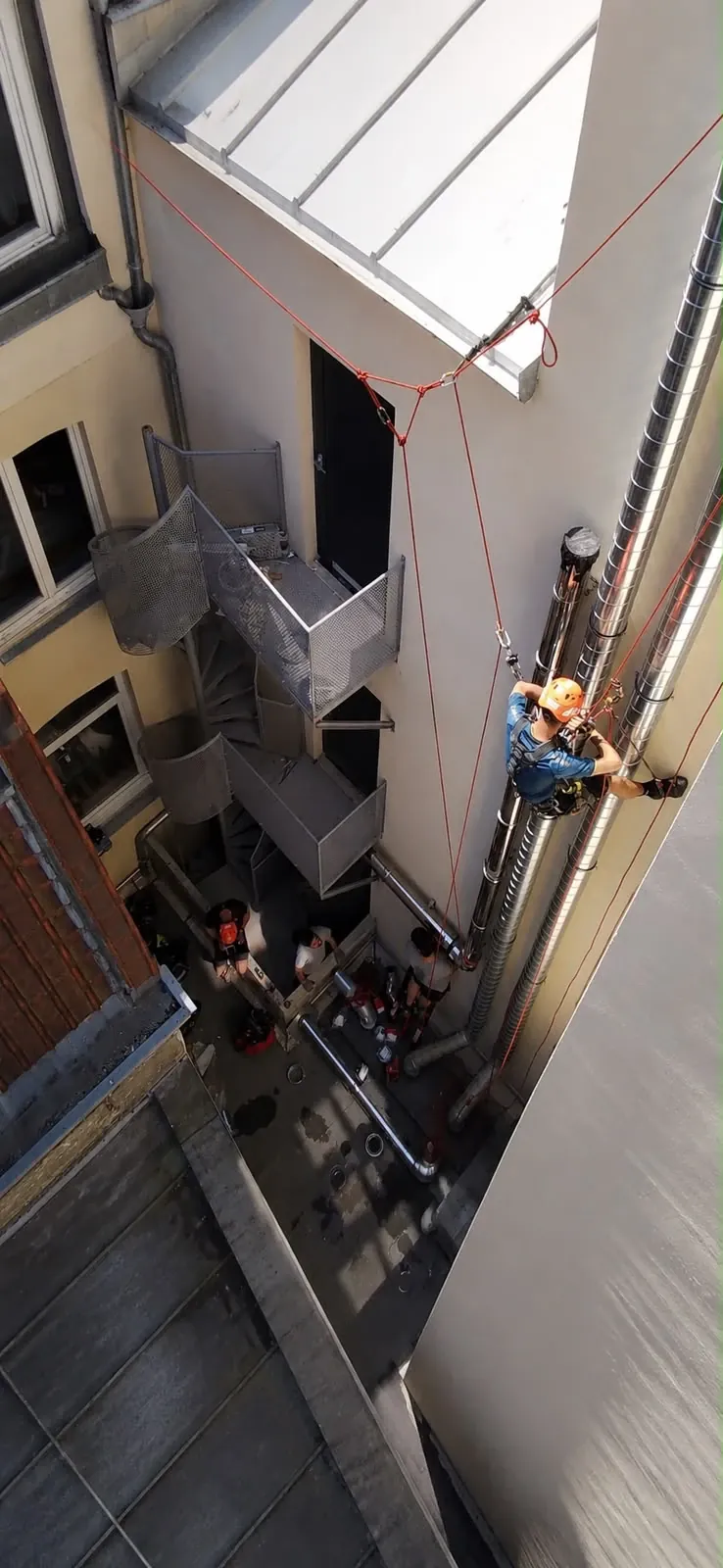 Cordiste posant des conduits le long d'une façade dans une cour intérieure